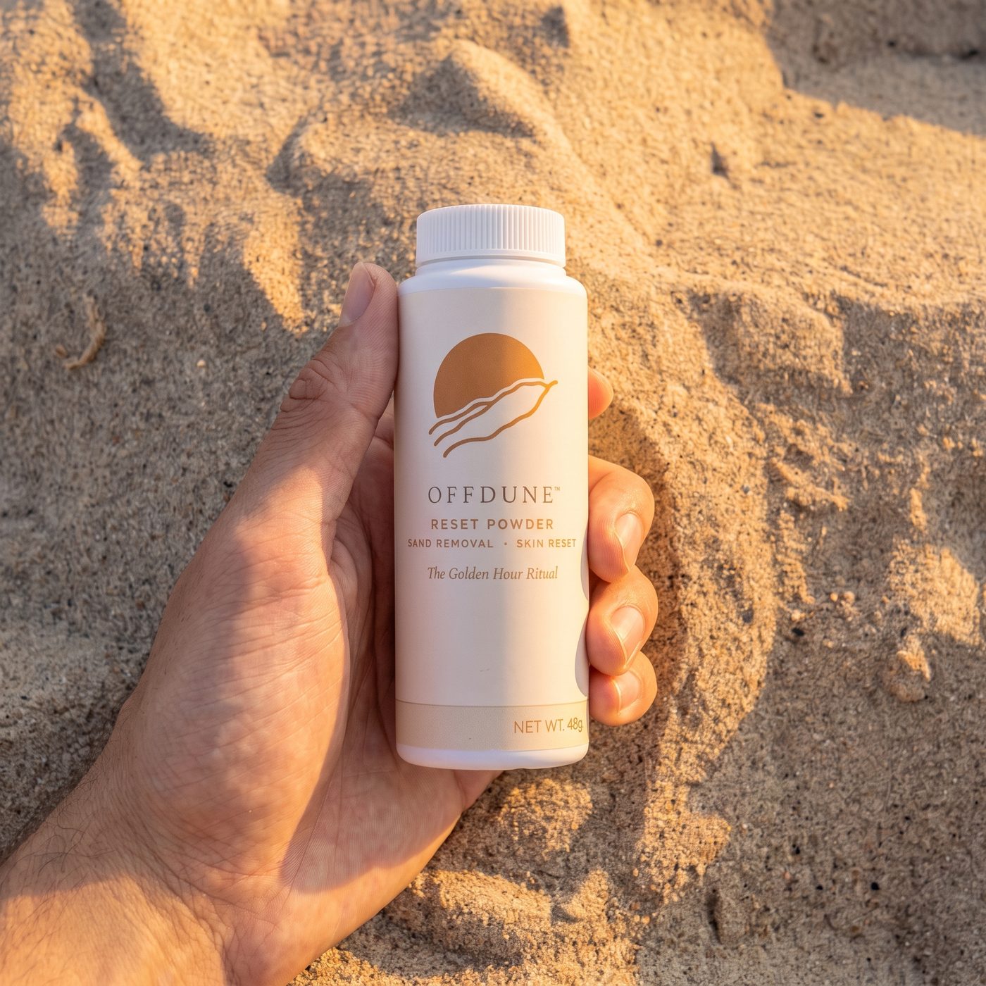 A hand holding the OFFDUNE Reset Powder bottle against golden-hour beach sand